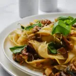 Pasta con crema di melanzane cremosa e dorata, guarnita con ricotta salata e pinoli tostati